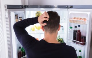 a man scratching his head in front of an open fridge