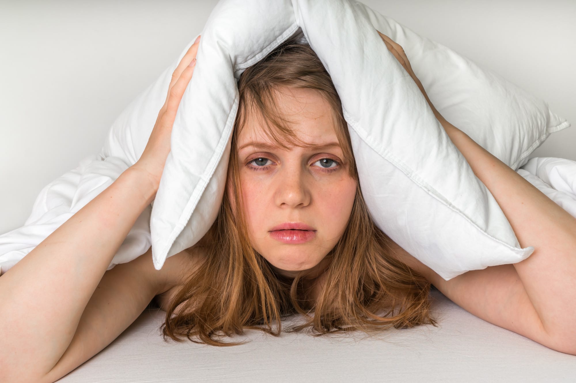 a woman holding a pillow over her ears